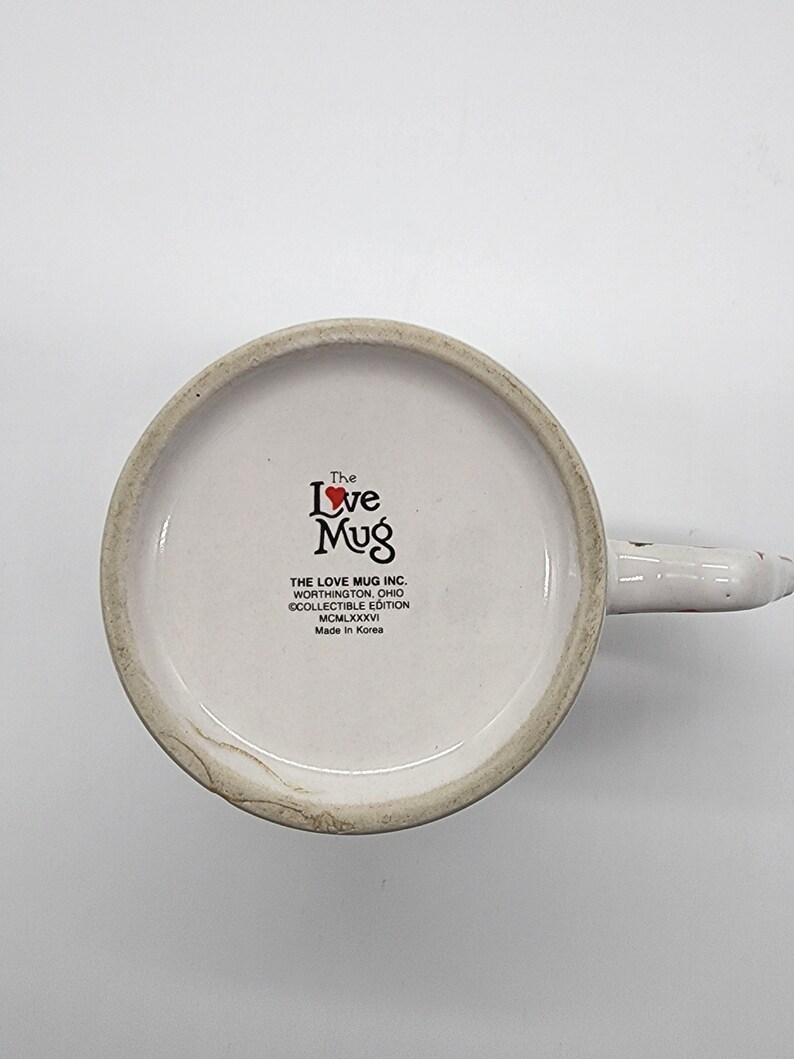 Puede incluir: Taza de cer&aacute;mica blanca con un coraz&oacute;n rojo y las palabras "The Love Mug" en negro. La taza tambi&eacute;n tiene el texto "THE LOVE MUG INC. WORTHINGTON, OHIO &copy;COLLECTIBLE EDITION MCMLXXXVI Made in Korea."