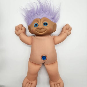 May include: A plush troll doll with purple hair and blue eyes. The doll has a blue gem on its belly button.