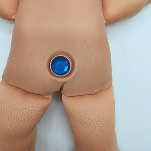May include: A close-up of a doll's back with a blue gem button.