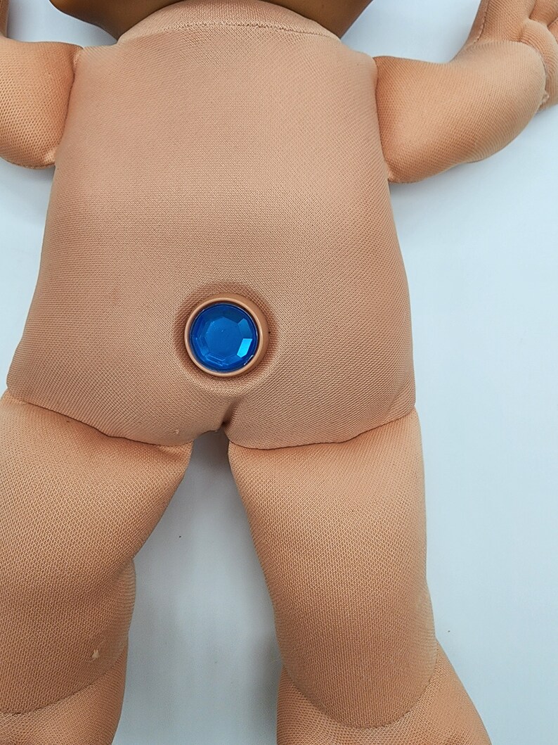 May include: A close-up of a doll's back with a blue gem button.