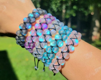 May include: A collection of beaded bracelets in various colors, including black, purple, blue, and pink. The bracelets are made of round, frosted beads woven together with black string. The beads have a glowing effect, creating a unique and eye-catching accessory.