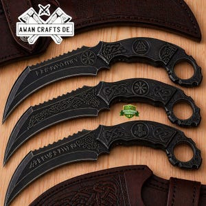 May include: Three black karambit knives with curved blades and intricate handle designs. Each knife features etched patterns and runes, with a ring at the end of the handle. The knives are displayed on a wooden surface with leather sheaths.
