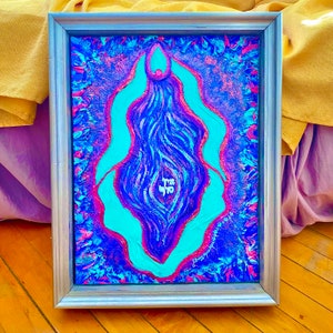May include: A framed abstract painting with a blue, purple, and pink color scheme. The painting features a central, teal-colored shape with a swirling, blue and purple pattern inside. The painting is signed in the bottom right corner.