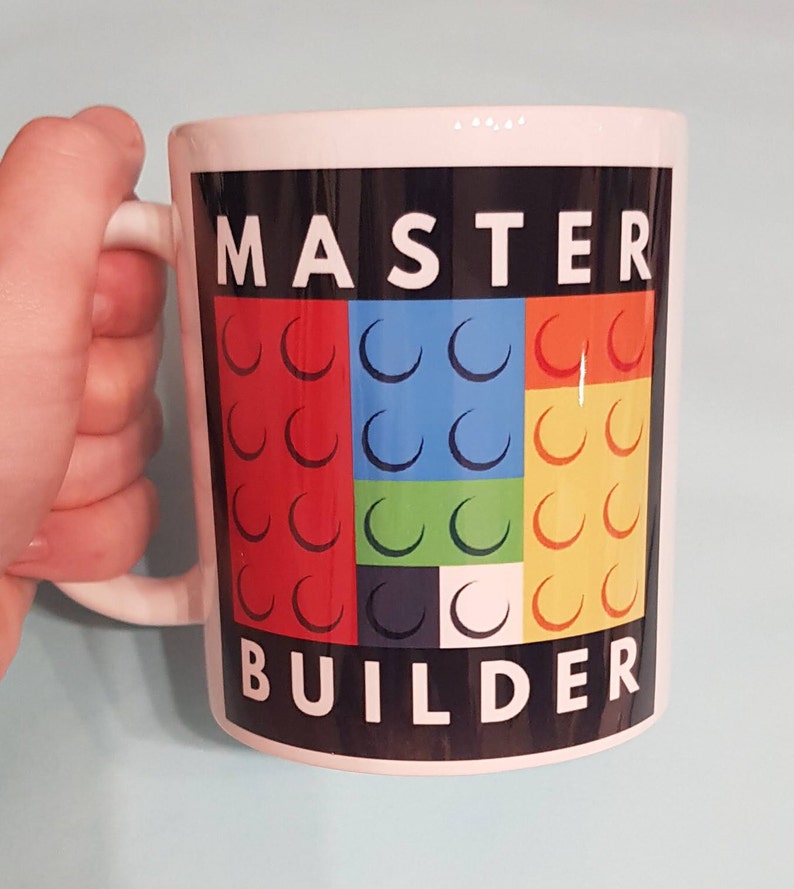 May include: White ceramic mug with a black background and the words "MASTER BUILDER" in white text. The background features a colorful design of nine red, blue, green, and yellow Lego bricks.