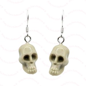 Puede incluir: Un par de pendientes de plata con un dije de calavera blanca. Las calaveras tienen un diseño detallado con cuencas de los ojos, una nariz y dientes.