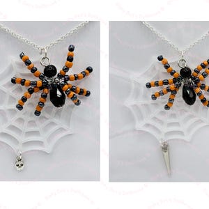 Könnte beinhalten: Ein schwarzer und orangefarbener Perlenspinnenanhänger an einer silbernen Kette mit einem weißen Plastikspinnennetz und einem Totenkopf-Anhänger.