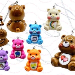 May include: A set of ten Care Bear charm necklaces. Each necklace features a different Care Bear character with a unique colour and design. The charms are made of plastic and have a shiny finish. The necklaces are silver chains.