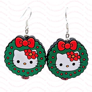 May include: A pair of green and red Christmas wreath earrings with a white Hello Kitty face in the centre.
