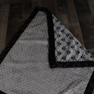 May include: A gray and black baby blanket with a skull and crossbones pattern on one side and a soft, textured fabric on the other side.