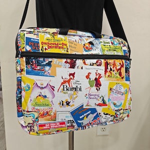 May include: A rectangular shoulder bag featuring a collage of vintage Walt Disney movie posters. The bag has a black strap and zipper, with colorful images from films like "Bambi," "Snow White," and "One Hundred and One Dalmatians."