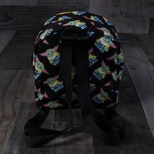 Puede incluir: Mochila negra con un patr&oacute;n repetido de un personaje verde y azul con las palabras "Star Wars" sobre un fondo negro.