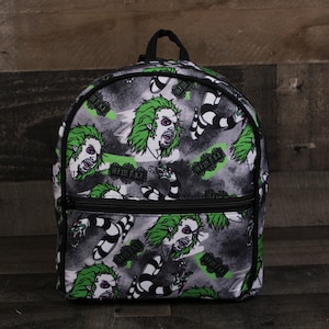 May include: A black backpack with a green and white print of a character with green hair and a striped shirt. The print repeats across the backpack. The text "Beetlejuice" is visible on the backpack.