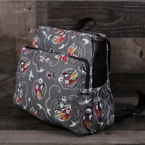 May include: A gray backpack with a black zipper and straps. The backpack has a repeating pattern of Jack Skellington and Sally from the Nightmare Before Christmas.