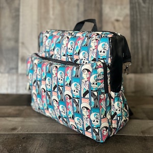 Puede incluir: Una mochila de patr&oacute;n azul y rosa con detalles negros. El patr&oacute;n presenta una imagen repetida de Jack Skellington y Sally de Pesadilla antes de Navidad.