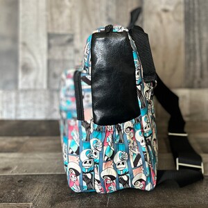 Puede incluir: Una mochila de patr&oacute;n azul y blanco con un bolsillo de cuero negro en la parte posterior. La mochila tiene una correa negra ajustable y un cierre de cremallera.