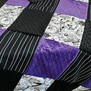 May include: A patchwork quilt featuring a variety of textures and patterns. The quilt incorporates black and white comic-style prints, black and white striped fabric, solid purple, and black textured fabric. The quilt has a black satin border.