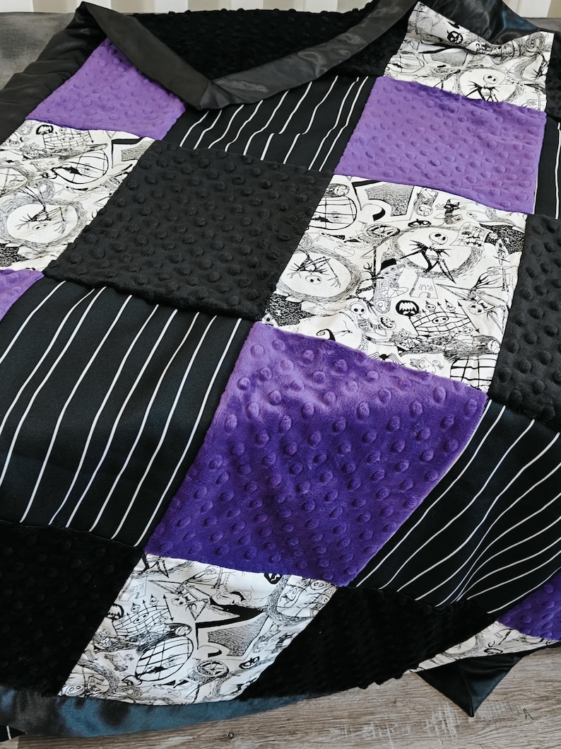 May include: A patchwork quilt featuring a variety of textures and patterns. The quilt incorporates black and white comic-style prints, black and white striped fabric, solid purple, and black textured fabric. The quilt has a black satin border.