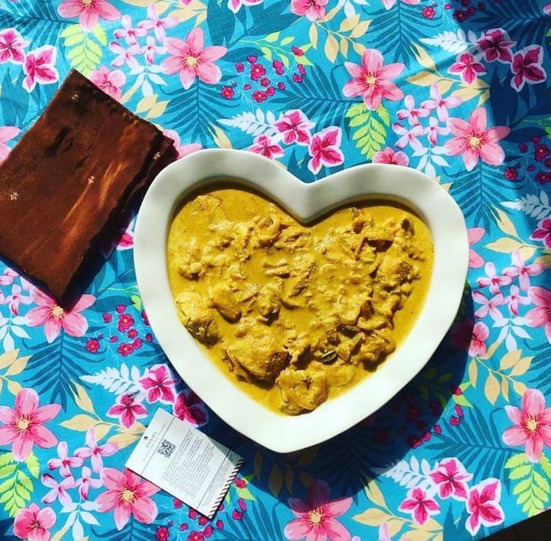 Peut inclure: Un plat de service en forme de c&oelig;ur blanc rempli d'un curry jaune cr&eacute;meux. Le plat est sur une nappe florale bleue et rose.