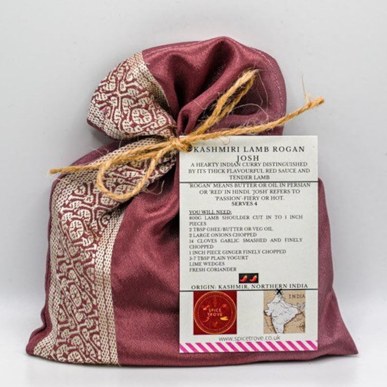 May include: A red and white patterned fabric pouch tied with twine and a recipe card for Kashmiri Lamb Rogan Josh. The card includes a map of India and the text "Kashmiri Lamb Rogan Josh, A hearty Indian curry distinguished by its thick flavorful red sauce and tender lamb. Rogan means butter or oil in Persian or 'red' in Hindi. Josh refers to passion-fiery or hot. Serves 4. You will need: 800g lamb shoulder cut in to 1 inch pieces, 2 tbsp ghee/butter or veg oil, 2 large onions chopped, 14 cloves garlic smashed and finely chopped, 1 inch piece ginger finely chopped, 5-7 tbsp plain yogurt, lime wedges, fresh coriander. Origin: Kashmir, Northern India. www.spicetrove.co.uk"