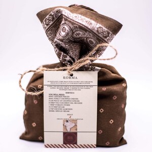 Peut inclure: Un sac en tissu brun avec une &eacute;tiquette indiquant "KORMA" et listant les ingr&eacute;dients et les instructions pour faire un curry korma. L'&eacute;tiquette comprend &eacute;galement le texte "SERVES 4" et "HEAT".
