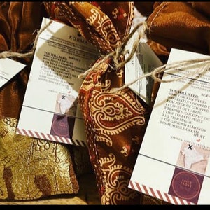 Peut inclure: Quatre petites pochettes en tissu brun avec des broderies dor&eacute;es, attach&eacute;es avec de la ficelle et &eacute;tiquet&eacute;es avec des cartes de recettes pour un plat Korma. Les cartes de recettes &eacute;num&egrave;rent les ingr&eacute;dients et les instructions pour pr&eacute;parer le plat. Les cartes ont une bordure ray&eacute;e rouge et blanche et un logo avec les mots "Spice Store" dans un cercle.