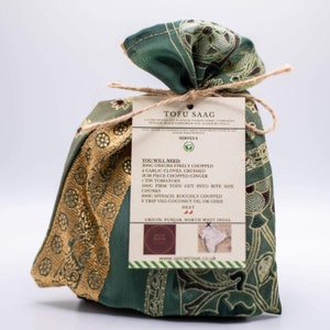 May include: A green and gold fabric pouch with a label that reads "Tofu Saag" and lists the ingredients needed to make the dish. The label also includes the text "Serves 4" and "Origin Punjab, North West India".