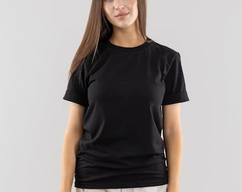 May include: A woman wearing a black short-sleeved t-shirt and beige pants.