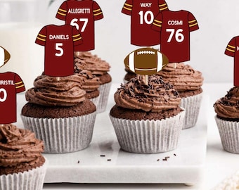 May include: A collection of chocolate cupcakes topped with paper decorations featuring burgundy football jerseys with yellow trim and white numbers, including names like Daniels 5, Allegretti 67, Way 10, Cosmi 76, Sainristil 0, and McLaurin 17, alongside brown football icons.