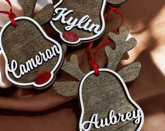 May include: Three wooden reindeer ornaments with red ribbon and glitter noses. The ornaments are personalised with the names "Cameron", "Kylin", and "Aubrey".