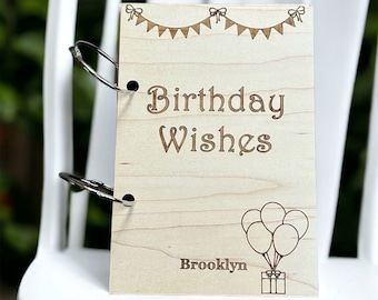 May include: A wooden book with a ring binder, personalized with the name "Brooklyn". The cover features the text "Birthday Wishes" and a design of balloons and a gift box.