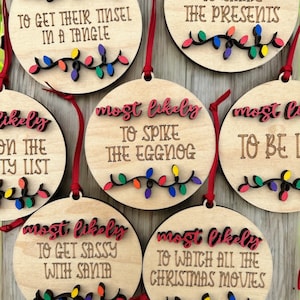 May include: Six wooden Christmas baubles with red and white text that reads "most likely" followed by a humorous Christmas-themed phrase. Each bauble has a string of colourful lights.