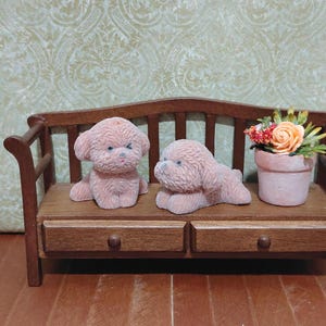May include: Miniature wooden bench with two pink poodle figurines and a small flower pot. The bench has a dark brown finish with two drawers. The poodles are sitting and lying down. The flower pot contains orange and red flowers.