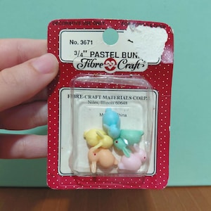 May include: A package of pastel bunny figurines in various colors, including pink, yellow, blue, green, and orange. The package is labeled "3/4" PASTEL BUN" and "Fibre Craft". The package is red with white polka dots and the text "DECORATIVE USE ONLY".
