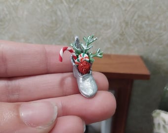 May include: A miniature silver shoe filled with Christmas decorations, including a candy cane, a red and white striped candy, and a red glitter ball.