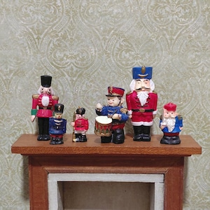 May include: A collection of miniature toy soldiers and nutcrackers in various poses. The figures are painted in bright colors, including red, blue, and black, and are arranged on a wooden shelf. The background features a patterned wallpaper.