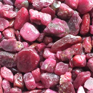 Könnte beinhalten: Nahaufnahme eines Haufens roher, ungeschliffener Rubin-Edelsteine. Die Steine variieren in Größe und Form und haben eine tiefrote Farbe und eine leicht raue Textur. Diese Natursteine eignen sich für die Schmuckherstellung.