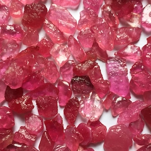 Puede incluir: Primer plano de una colección de gemas de rubí en bruto. Las piedras, de diferentes tamaños y formas, presentan tonos rosados y rojizos. Se aprecia la textura rugosa y las formas naturales de las piedras.