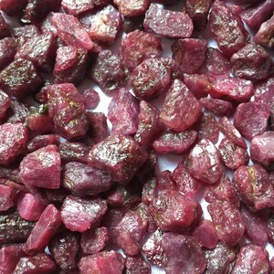 Könnte beinhalten: Nahaufnahme einer Ansammlung von rohen Rubin-Edelsteinen. Die Steine haben eine tiefe rote Farbe mit unterschiedlichen Schattierungen und Texturen. Die Edelsteine sind unregelmäßig geformt und scheinen unpoliert. Geeignet für Schmuckherstellung oder als Dekoration.