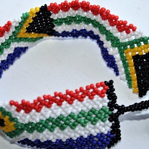 May include: A beaded bracelet featuring the colours of the South African flag. The bracelet is made from small, colourful beads and has a black tassel.
