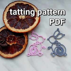 May include: Two crocheted bunny patterns in pink and gray. The patterns are on a white surface with dried orange slices and a star anise.