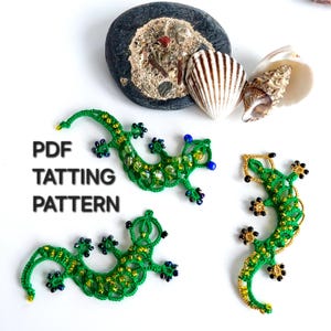 May include: Three green lizard-shaped tatting lace motifs embellished with small beads in yellow, blue, and black. The text PDF TATTING PATTERN is printed in black on the left side. A dark grey stone and two seashells are positioned at the top.