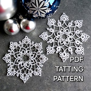 Peut inclure: Deux flocons de neige en crochet blanc, l'un plus grand que l'autre, sur un fond gris. Le texte "PDF TATTING PATTERN" est imprimé sous les flocons de neige.