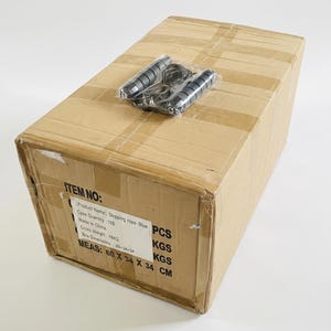 May include: A brown cardboard shipping box with a skipping rope in clear plastic packaging on top. The box features a printed label with the text: ITEM NO: Product Name: Skipping rope-Blue, Case Quantity: 100 PCS, Made in China, Cross Weight: 18KG, Box Dimensions: 60x34x34, MEAS: 60 X 34 X 34 CM.