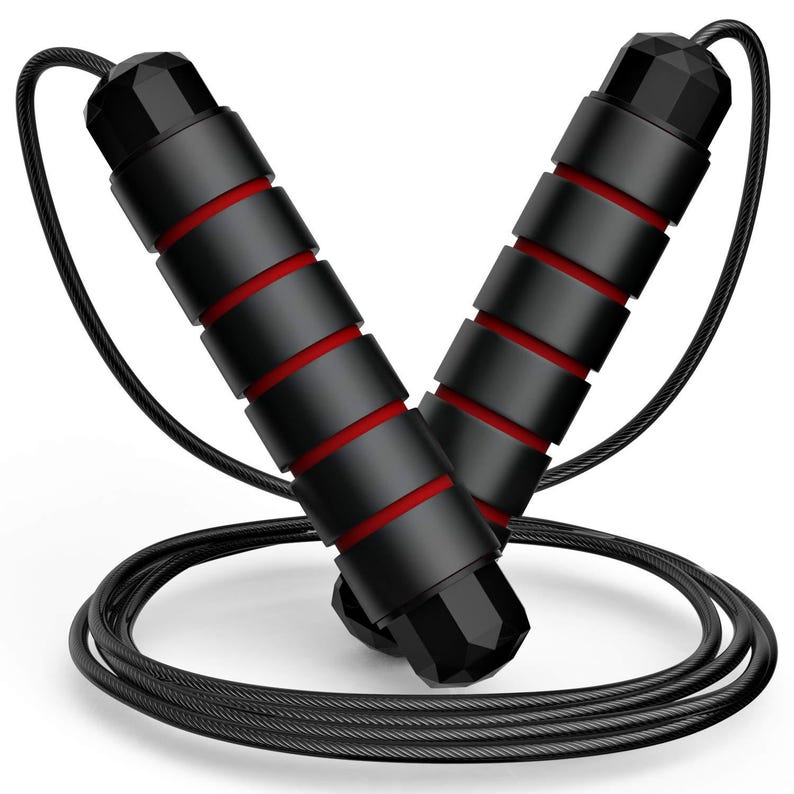 May include: A jump rope featuring two black handles with red accents and a textured grip. The handles are connected by a thin, black, flexible cable that coils at the base. The design includes faceted black end caps on both of the handles.