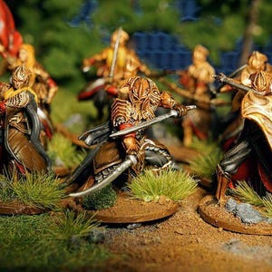 K&ouml;nnte beinhalten: Eine Gruppe von f&uuml;nf Miniaturfiguren, die in Gold und Rot bemalt sind, sind in Kampfformation aufgestellt. Die Figuren halten Schwerter und Schilde und stehen auf einer grasbewachsenen Oberfl&auml;che.