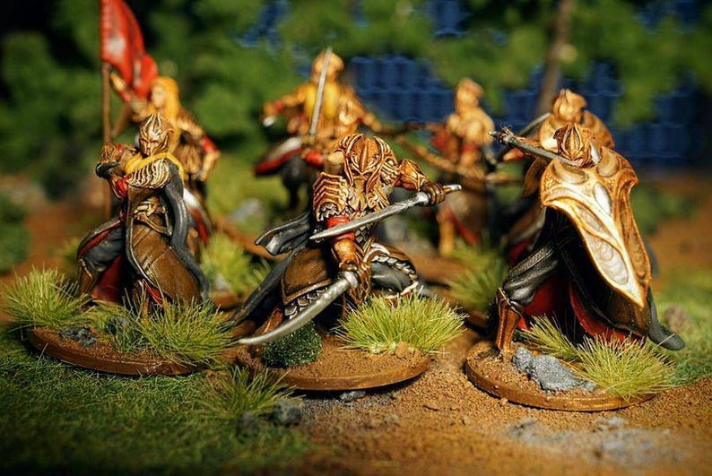 K&ouml;nnte beinhalten: Eine Gruppe von f&uuml;nf Miniaturfiguren, die in Gold und Rot bemalt sind, sind in Kampfformation aufgestellt. Die Figuren halten Schwerter und Schilde und stehen auf einer grasbewachsenen Oberfl&auml;che.