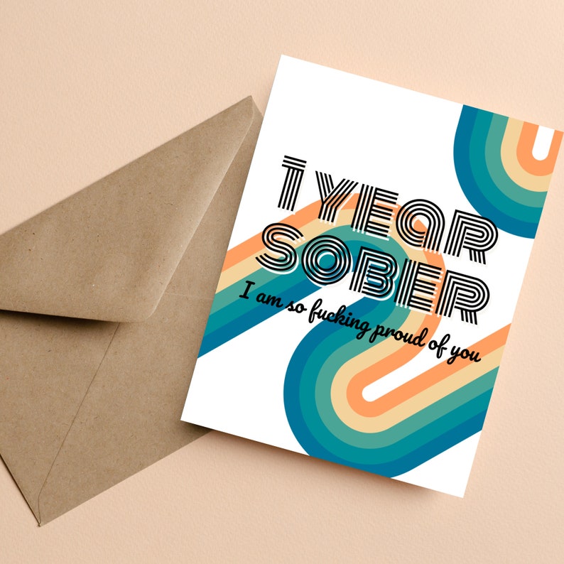Op de afbeelding: Een witte kaart met een kleurrijk regenboogontwerp en de tekst "1 YEAR SOBER I am so fucking proud of you".