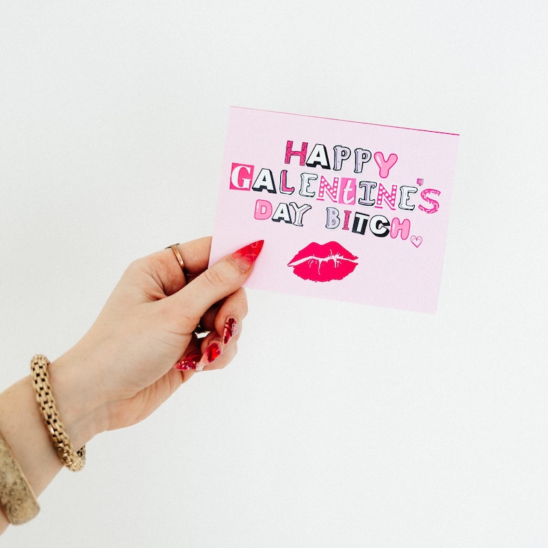 May include: Pink card with the text "Happy Galentine's Day Bitch" in pink and black letters with a pink heart and a pink lipstick print.