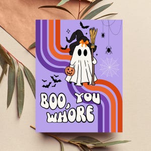 May include: A Halloween-themed greeting card with a purple background and retro orange and purple stripes. The card features a cartoon ghost wearing a witch hat and holding a broom and jack-o'-lantern. The text on the card reads "BOO, YOU WHORE."