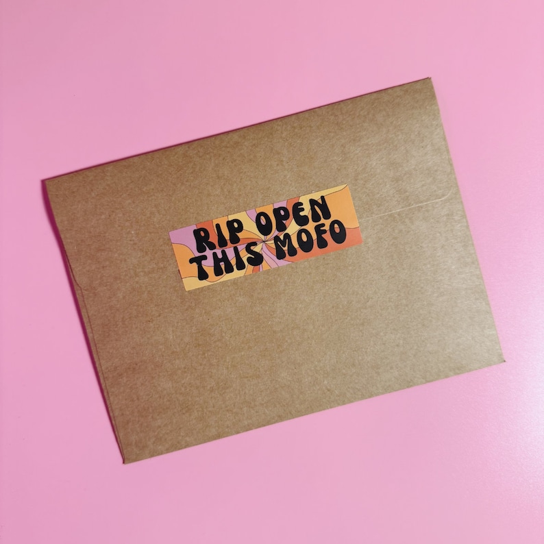 Puede incluir: Un sobre de papel marr&oacute;n con una pegatina colorida que dice "RIP OPEN THIS MOFO" en texto negro.